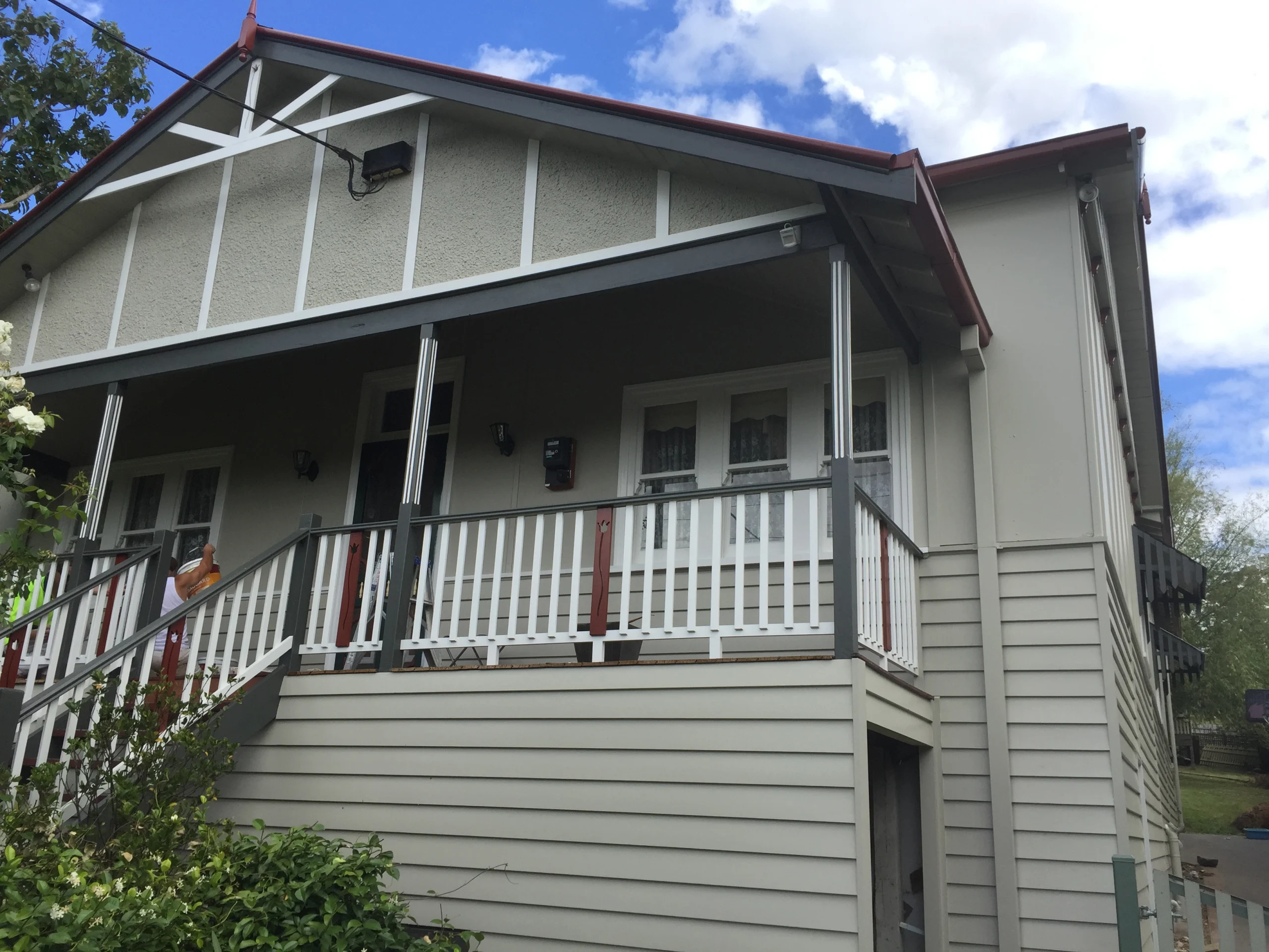 Repainted weatherboard home with white trim, charcoal verandah posts and a painter at work