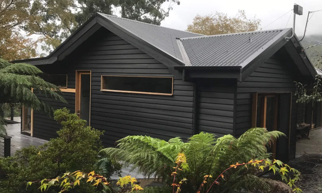 Charcoal weatherboard cottage among tree ferns in the Yarra Ranges